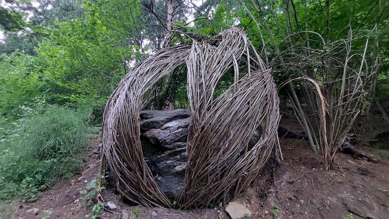 Eine geflochtene Weidenhütte im grünen Wald nahe einem großen Felsvorsprung.